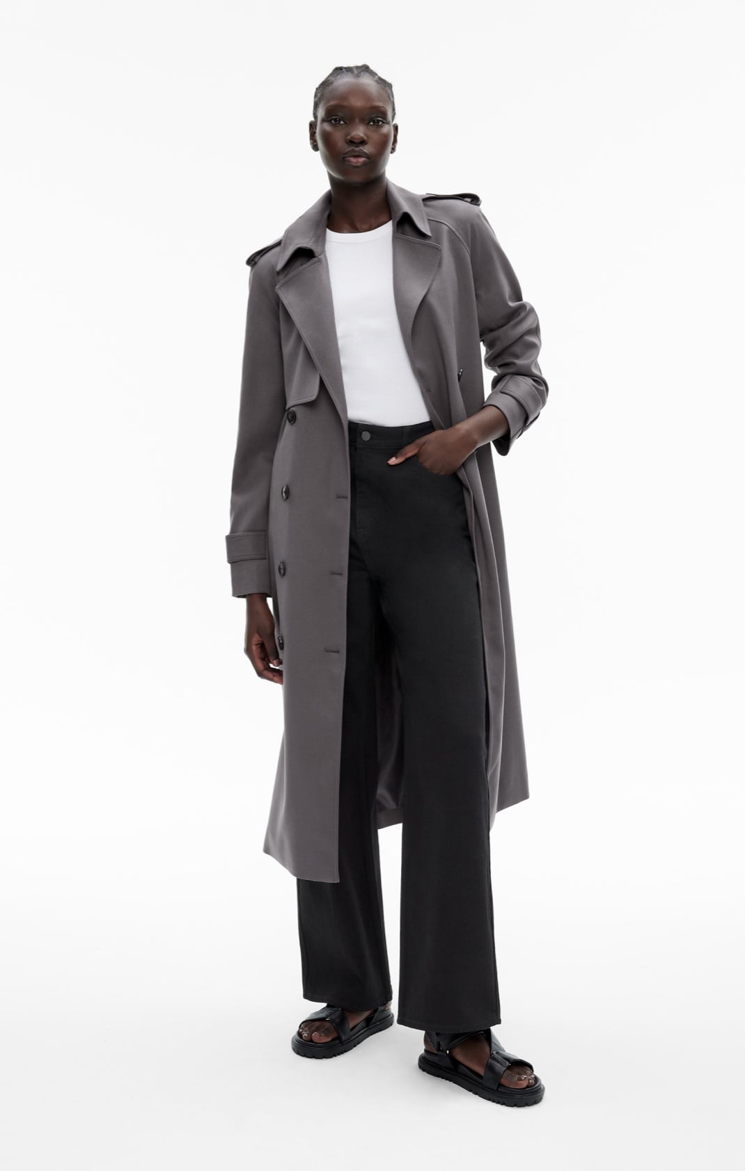 Woman in a grey trench coat, white t-shirt, black jeans and black sandals