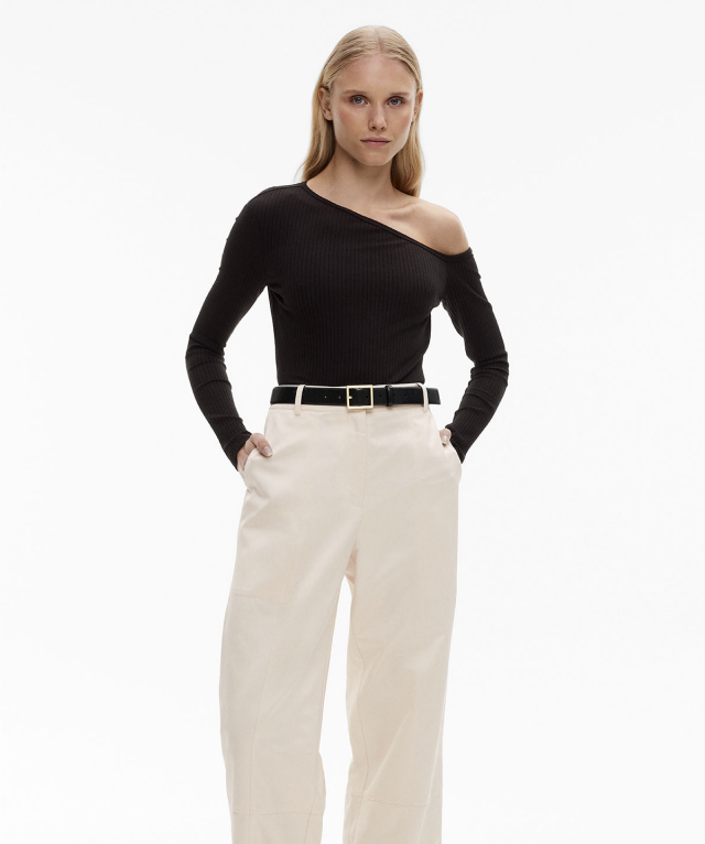 Woman in black long sleeve off shoulder top, white denim jeans and black leather belt