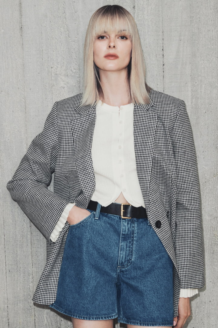 Woman in black linen check double breasted blazer, fresh white wool blend button front knit, indigo denim short and black saskia leather belt
