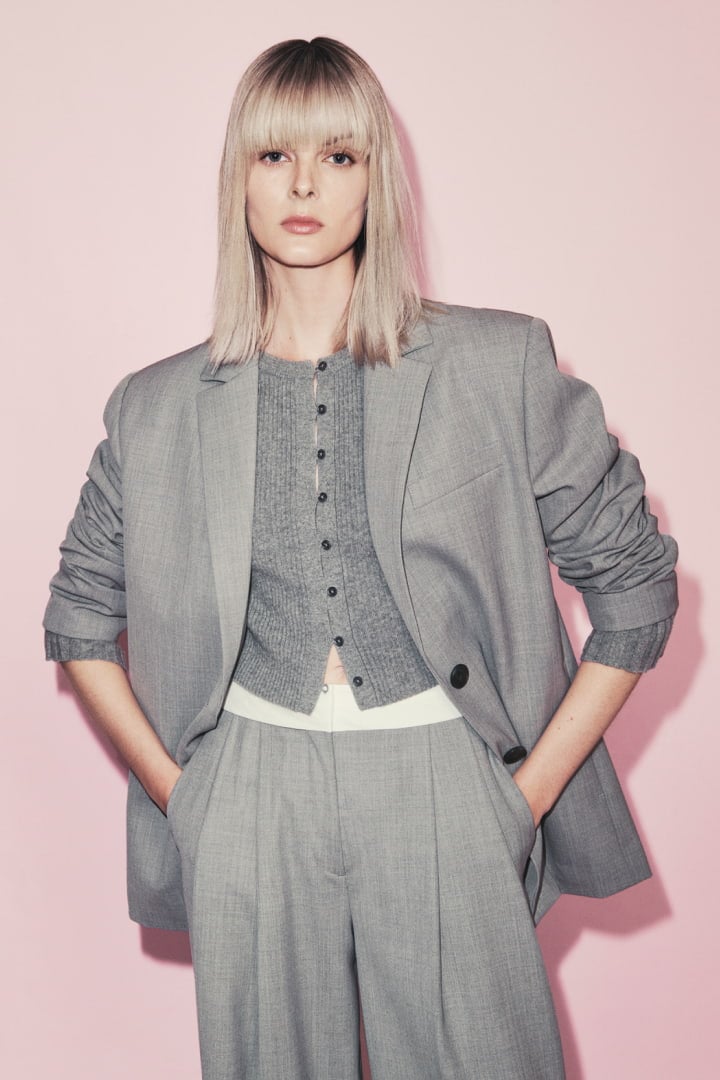 Woman in pale grey melange boxy single breasted blazer, pale grey wool blend button front knit and pale grey waist detail pant