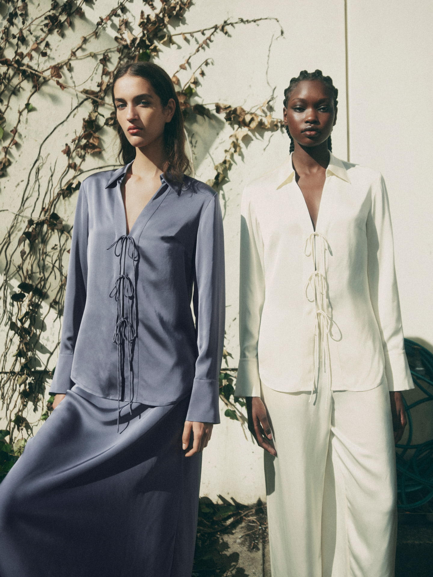 Woman on the left wearing the slate blue tie detail shirt and slate blue bias maxi slip skirt. Woman on the right wearing the vanilla tie detail shirt and vanilla fine waistband pant