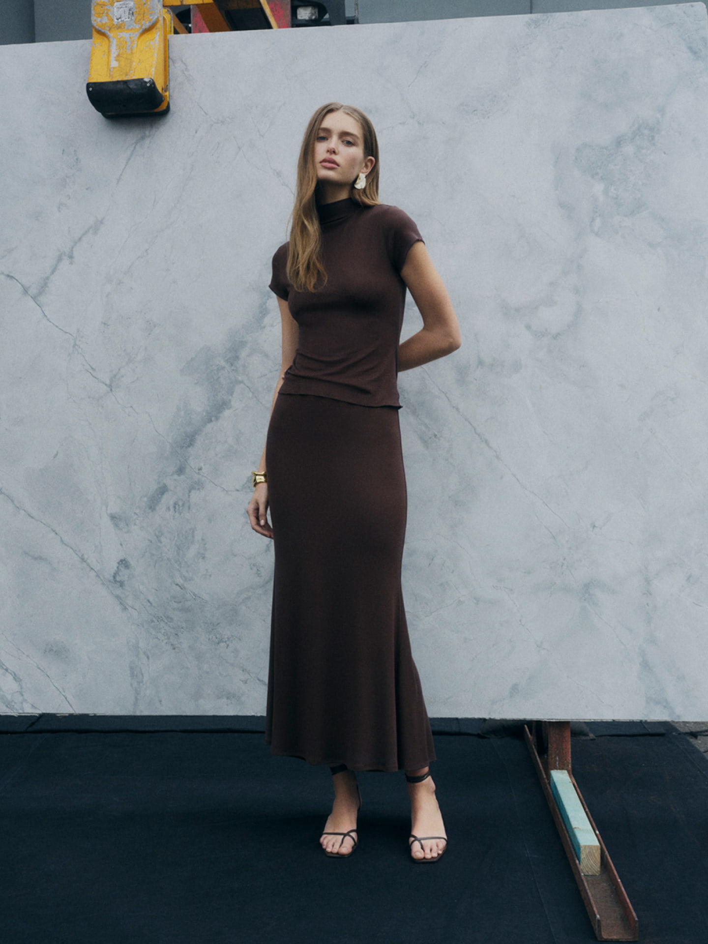 Woman in brown high neck cap sleeve tee, brown jersey maxi skirt and brown blair tie up heel