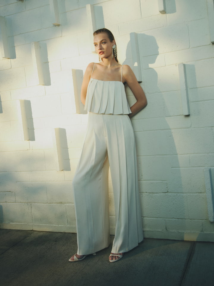Woman in chalk pleat cami, chalk pleat pants, eggshell isla wedge and gold poppy drop earrings